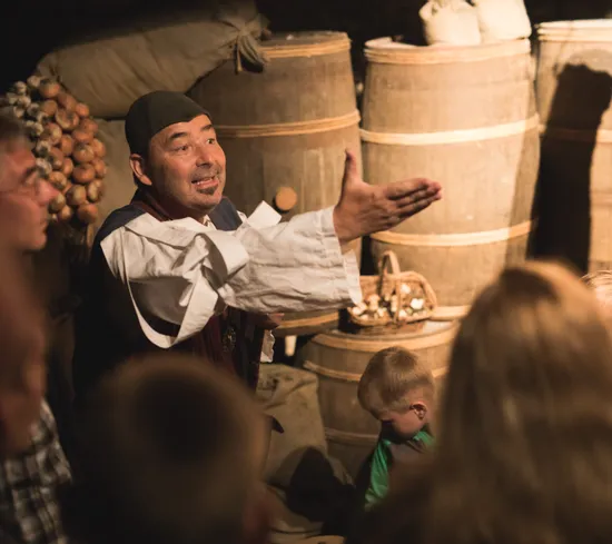 Historischer Darsteller erklärt einer Gruppe von Kindern und Erwachsenen ein mittelalterliches Lager